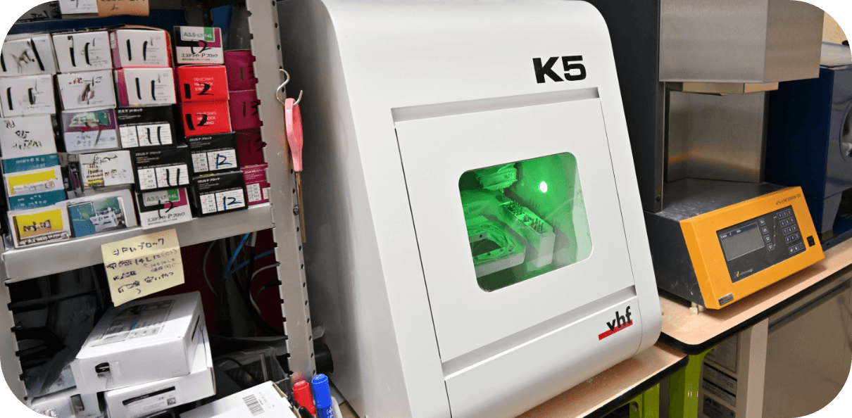 緑色の光が内部で点灯している「K5」モデルの歯科用ミリングマシンの画像