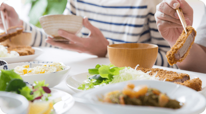 食卓に並ぶとんかつやサラダを囲んで、食事を楽しむ人々の様子